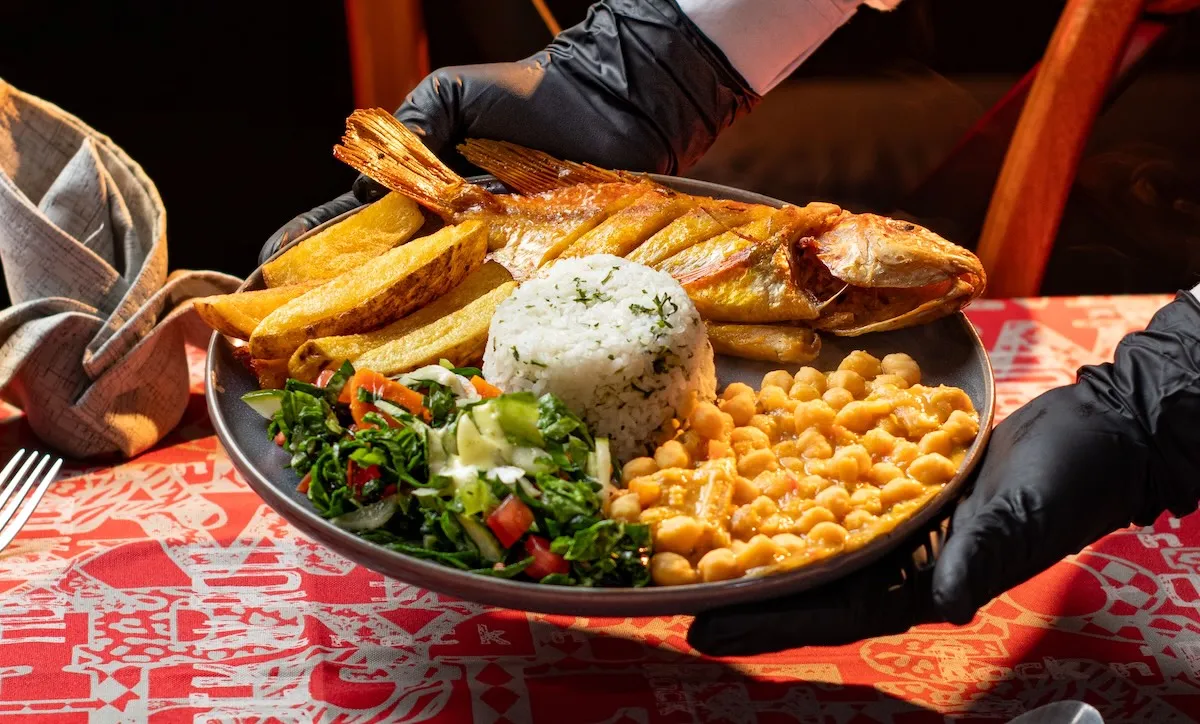 Ein Kellner serviert gebratenen Fisch mit Reis, Kartoffelecken, Kichererbsen und Salat in einem Restaurant in Hurghada